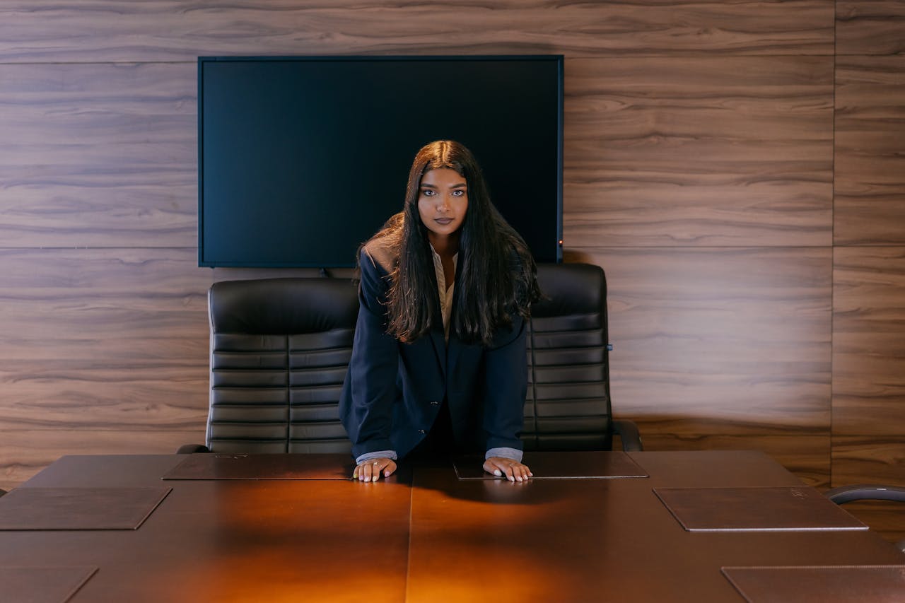 A confident businesswoman stands at a conference table in a modern office setting.